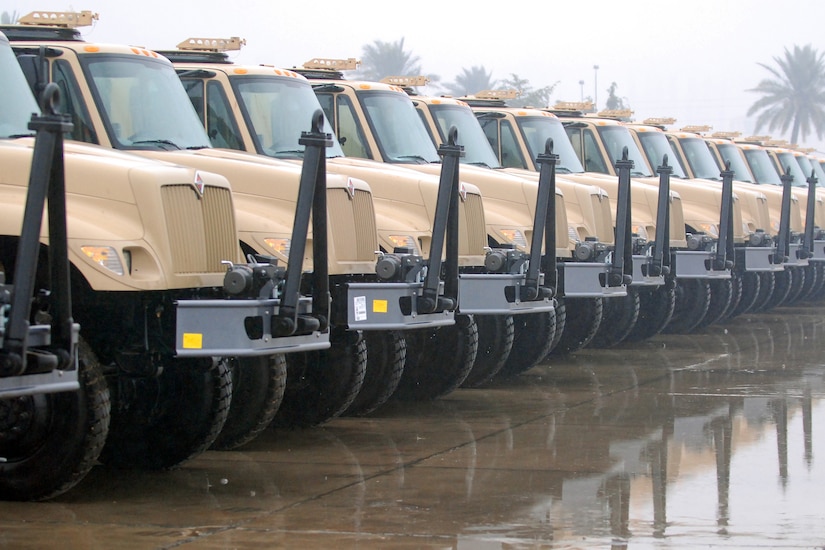 More than a dozen military vehicles sit side-by-side on a concrete slab.