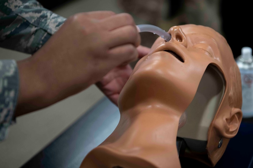 Airmen wearing face masks practice inserting a nasopharyngeal tube in a dummy.