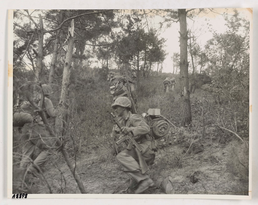 Men in combat uniform make their way up a heavily forested hill.