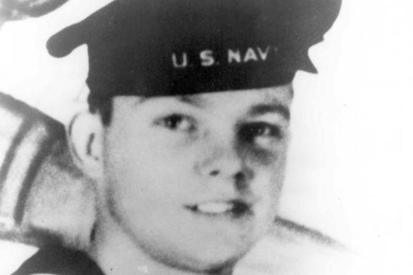 A young sailor in a Navy uniform and flat-top cap poses for a photo.
