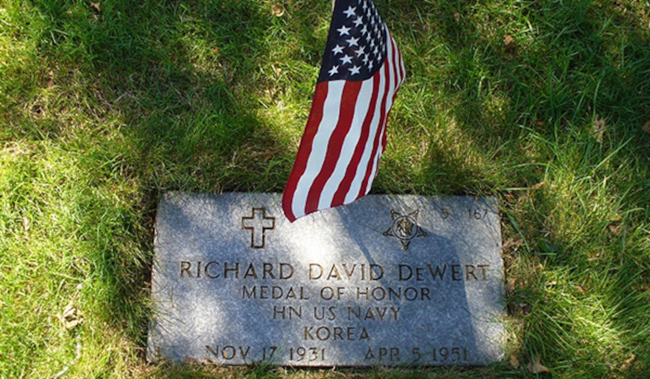 A grave marker on  the ground in a cemetery is decorated with a small American flag.