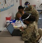 Spc. Nadiah Sims, foreground, confirms details about the vaccine and the patient's card while Spc. Han Thach sterilizes and administers the vaccine at Capital Area Intermediate Unit in Enola, Pa., on March 26, 2021.