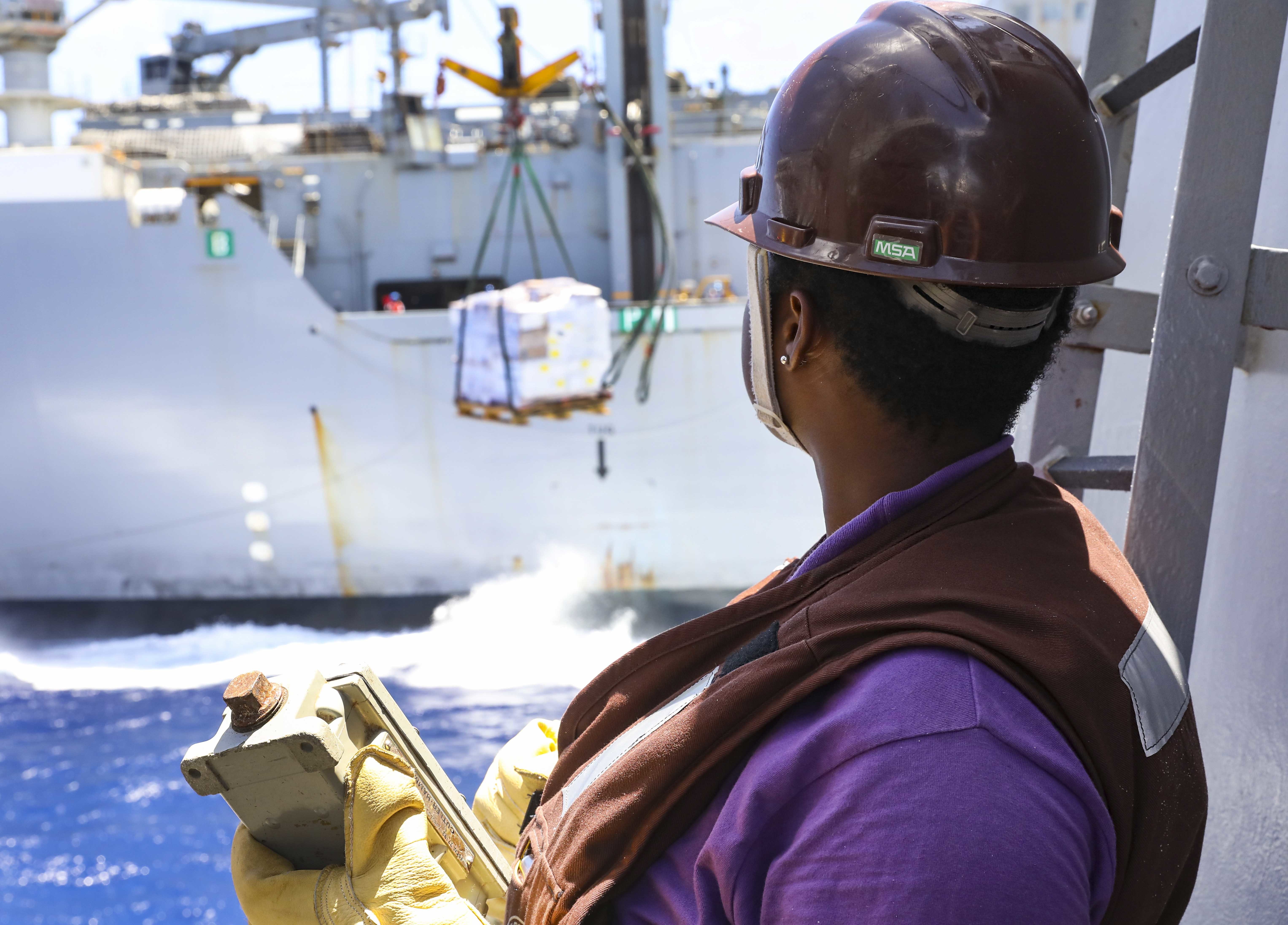 A Ssailor observes a pallet of supplies crossing from USNS Amelia Earhart (T-AKE 6) to the deck of USS Benfold (DDG 65) during a replenishment-at-sea.