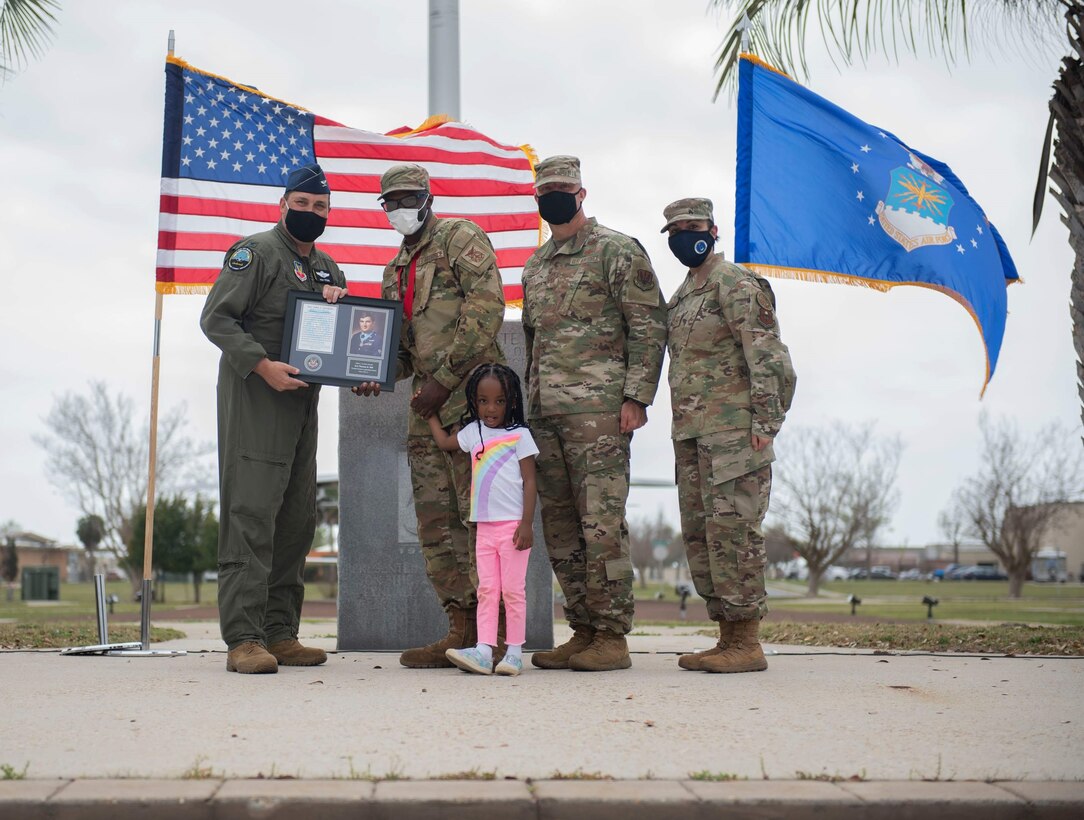 An Airman accepts his award from leadership while holding his daughter's hand.