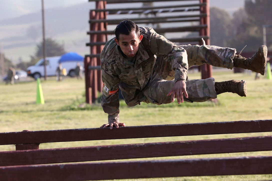 A guardsman jumps over a hurdle on an obstacle course.
