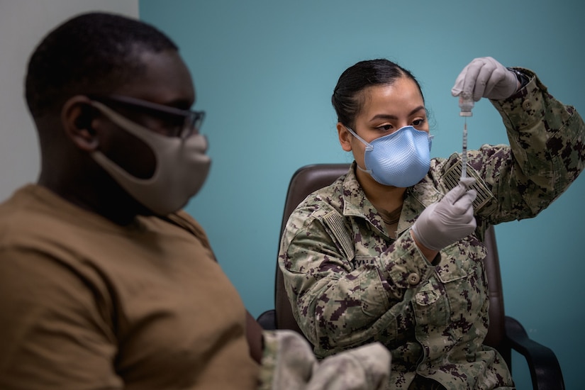 A sailor wearing gloves and a face mask prepares to vaccinate another sailor.