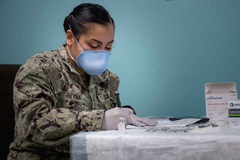 A sailor wearing a face mask and gloves fills out vaccine paperwork.