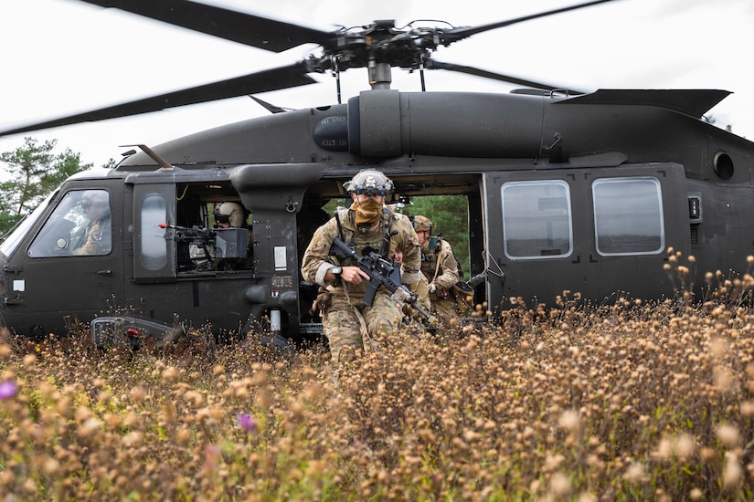 Troops exit helicopter in tall grass and weeds.