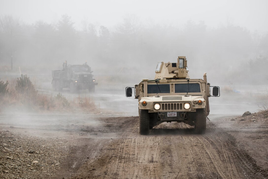 A Humvee and another vehicle drive along a dusty road.