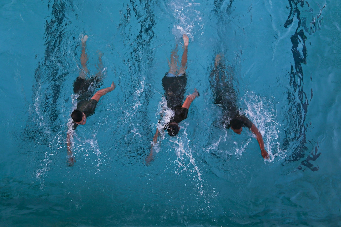 Three Marines swim in a pool.