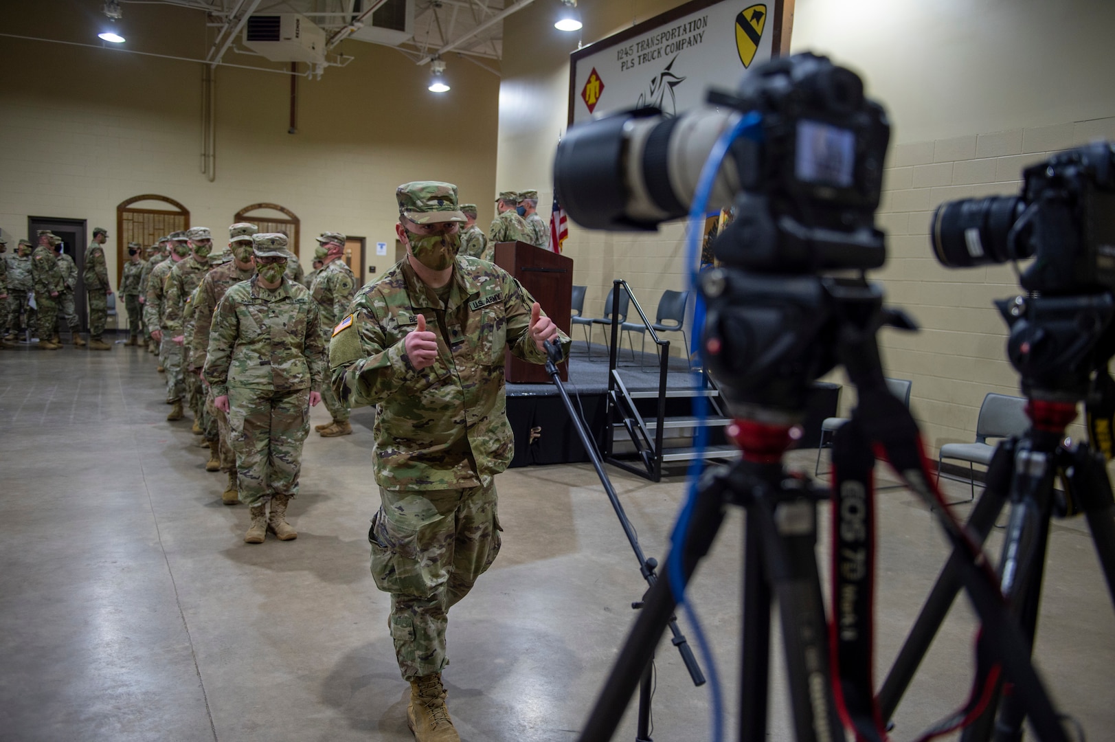A Soldier with the 345th Combat Sustainment Support Battalion gives a "thumbs up" gesture to cameras broadcasting a virtual send-off ceremony at the National Guard armory in Ada, Oklahoma, April 1, 2021. The Soldiers are being mobilized to Fort Bliss, Texas in order to provide COVID mitigation support to units deploying overseas. (Oklahoma National Guard photo by Leanna Maschino)