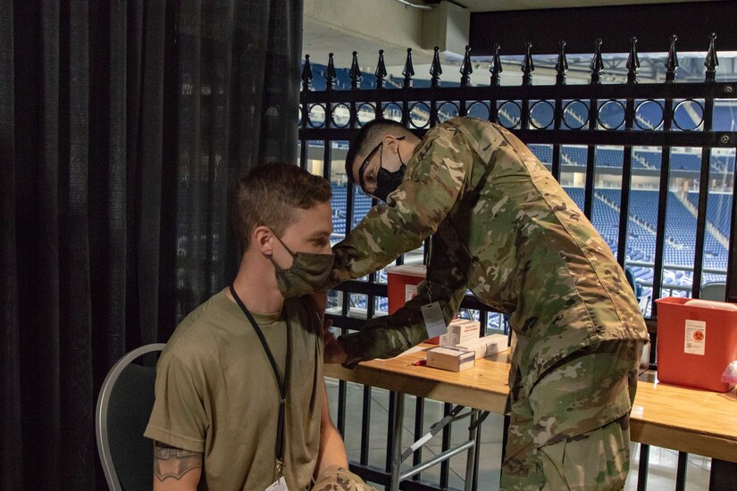 U.S. Air Force Senior Airman Dominic Patel, a Jonesboro, Arkansas, native and Aerospace Medical service member, part of the 88th Health Care Operations Squadron, stationed at Wright-Patterson Air Force Base, Ohio, acts out the vaccination procedure on Airman 1st Class Andrew Trempus, a Tyler, Texas, native and Aerospace Propulsion service member, part of the 35th component maintenance squad, stationed at Davis-Monthan Air Force Base, Arizona, at the state-run, federally-supported Ford Field COVID-19 Community Vaccination Center, March 22, 2021. Both Airmen are currently assigned to the 1st Detachment, 64th Air Expeditionary Group. The exercise covered all aspects of what a community member would experience upon arrival, through the entire vaccination process, at the CVC. U.S. Northern Command, through U.S. Army North, remains committed to providing flexible Department of Defense support to the whole-of-government COVID-19 response. (U.S. Army photo by Spc. Andrew Wash, 5th Mobile Public Affairs Detachment)