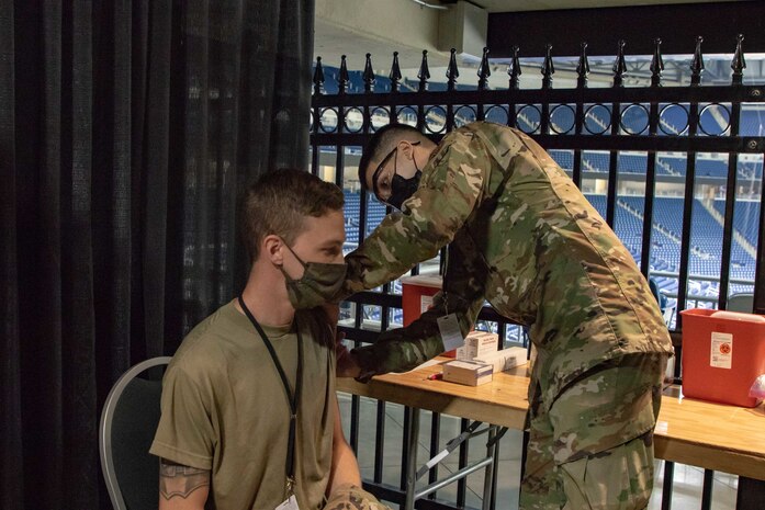 U.S. Air Force Senior Airman Dominic Patel, a Jonesboro, Arkansas, native and Aerospace Medical service member, part of the 88th Health Care Operations Squadron, stationed at Wright-Patterson Air Force Base, Ohio, acts out the vaccination procedure on Airman 1st Class Andrew Trempus, a Tyler, Texas, native and Aerospace Propulsion service member, part of the 35th component maintenance squad, stationed at Davis-Monthan Air Force Base, Arizona, at the state-run, federally-supported Ford Field COVID-19 Community Vaccination Center, March 22, 2021. Both Airmen are currently assigned to the 1st Detachment, 64th Air Expeditionary Group. The exercise covered all aspects of what a community member would experience upon arrival, through the entire vaccination process, at the CVC. U.S. Northern Command, through U.S. Army North, remains committed to providing flexible Department of Defense support to the whole-of-government COVID-19 response. (U.S. Army photo by Spc. Andrew Wash, 5th Mobile Public Affairs Detachment)