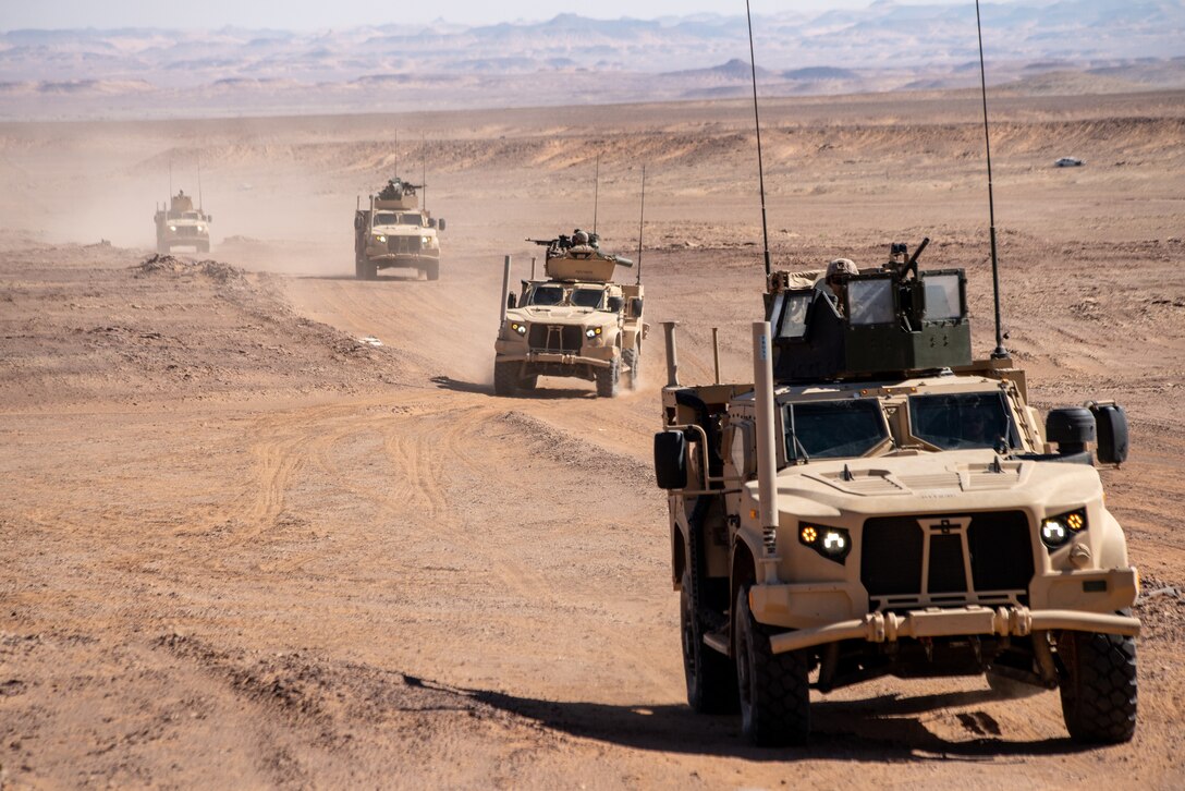 Marine Corps vehicles drive on desert-like terrain.