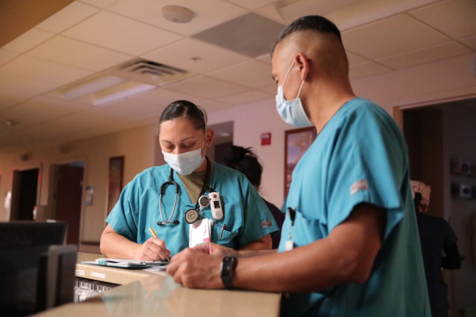 Two nurses wearing medical attire speak at a counter.