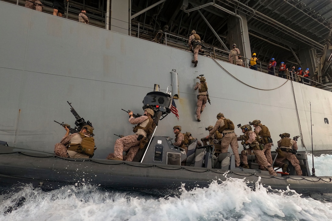 Marines climb a ladder from a small boat onto a ship while carrying weapons.