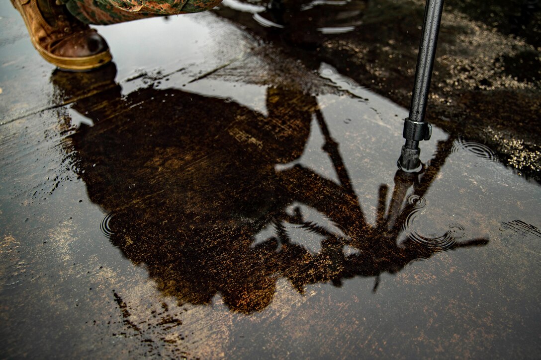 A Marine holds weapon as seen through a puddle on the ground.