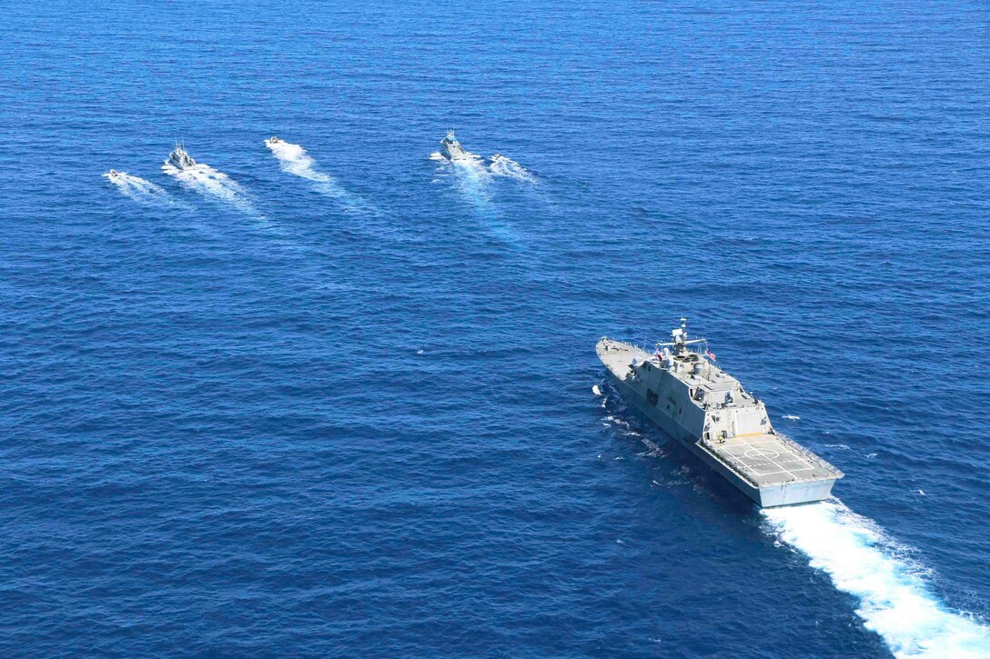 A large ship sails through waters behind five smaller vessels.