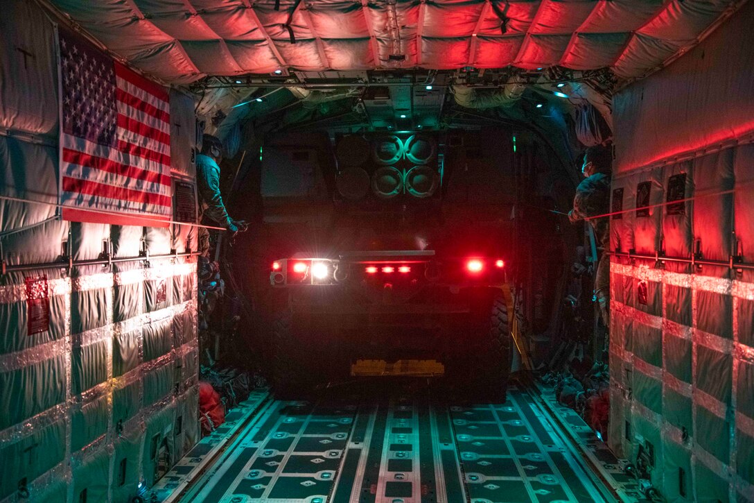 Airmen stand on either side of a high mobility artillery rocket system inside an aircraft.