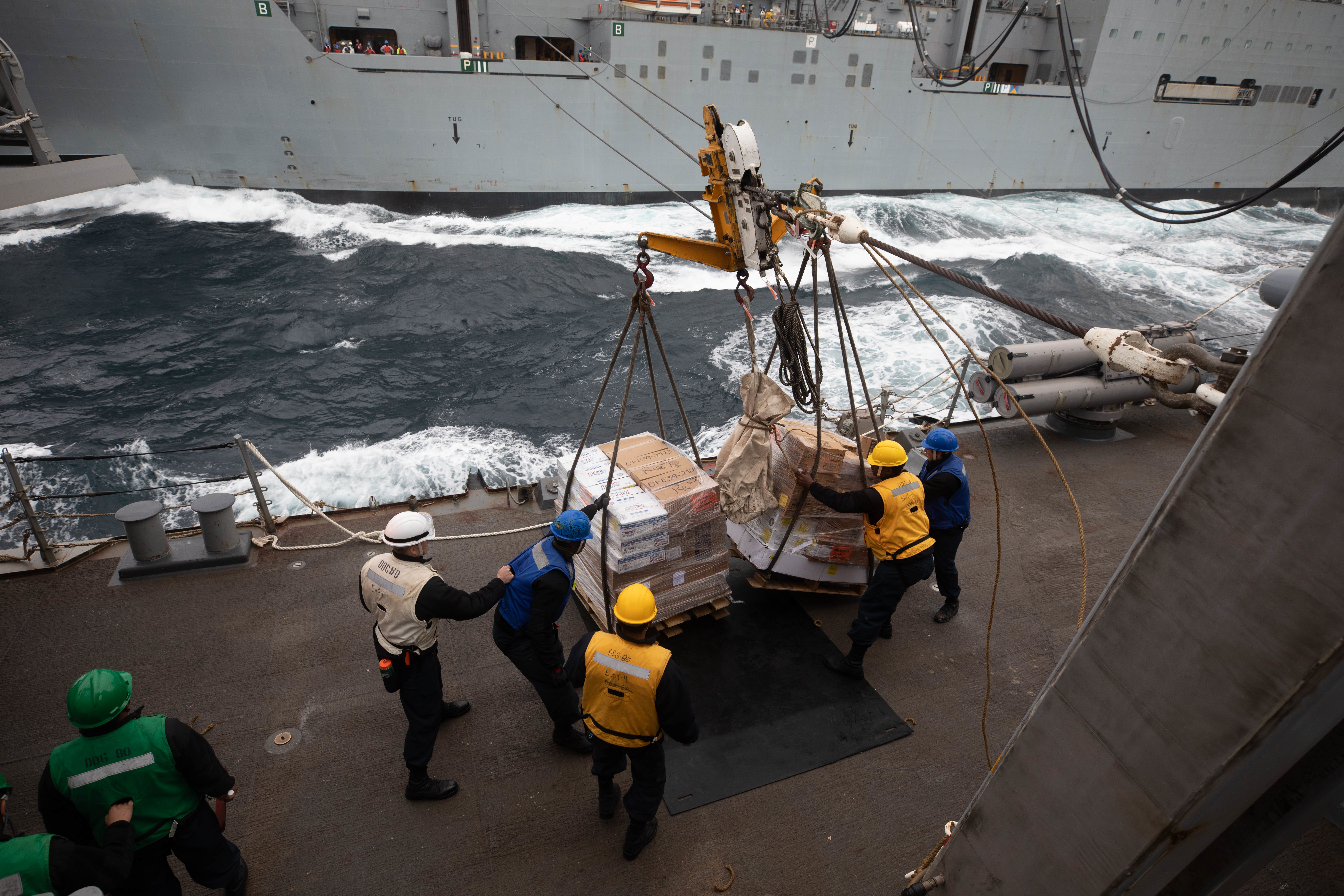 Sailors aboard the Arleigh Burke-class guided-missile destroyer USS Roosevelt (DDG 80) receive pallets of food stores during a replenishment-at-sea with the dry cargo ship USNS William McClean (T-AKE 12), April 1, 2021.