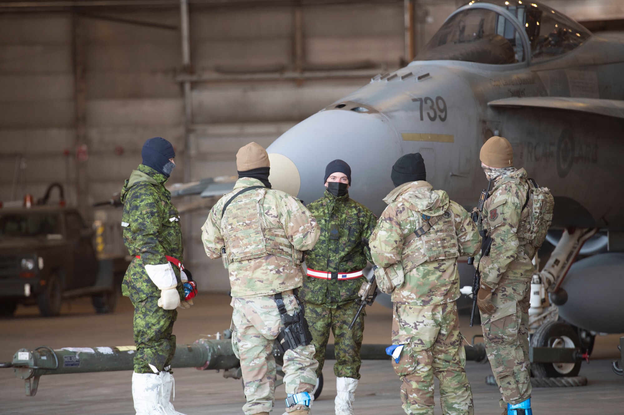 Airmen from the Minnesota Air National Guard and the Royal Canadian Air Force talk together in front of a Royal Canadian Air Force F-18 Hornet in a hangar at Thule Air Base, Greenland during North American Aerospace Defense Command’s Arctic air defense exercise, Amalgam Dart 21-02, March 23, 2021. (U.S. Air National Guard photo by 2nd Lt. Crystal Kirchner)