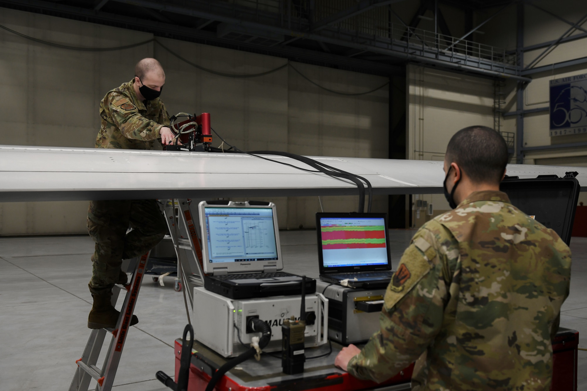 Airman First Class Seth Hardy, left/right, 319th Aircraft Maintenance Squadron nondestructive inspection journeyman, works alongside Senior Airman Harry Fraticelli, 319 AMXS NDI craftsman, to perform a scan using sound waves on the wing of an RQ-4 Global Hawk at Grand Forks Air Force Base, N.D., March 25, 2021. The scan is performed using a mobile automated scanner system as routine maintenance on the Global Hawk after every 150 flights. (U.S. Air Force photo by Airman 1st Class Ashley Richards)