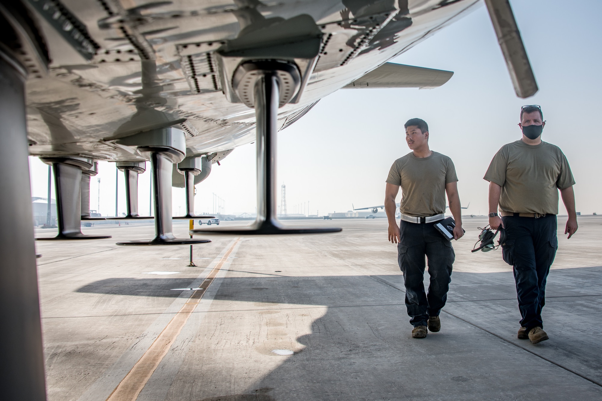 two men walk by the tail of an aircraft