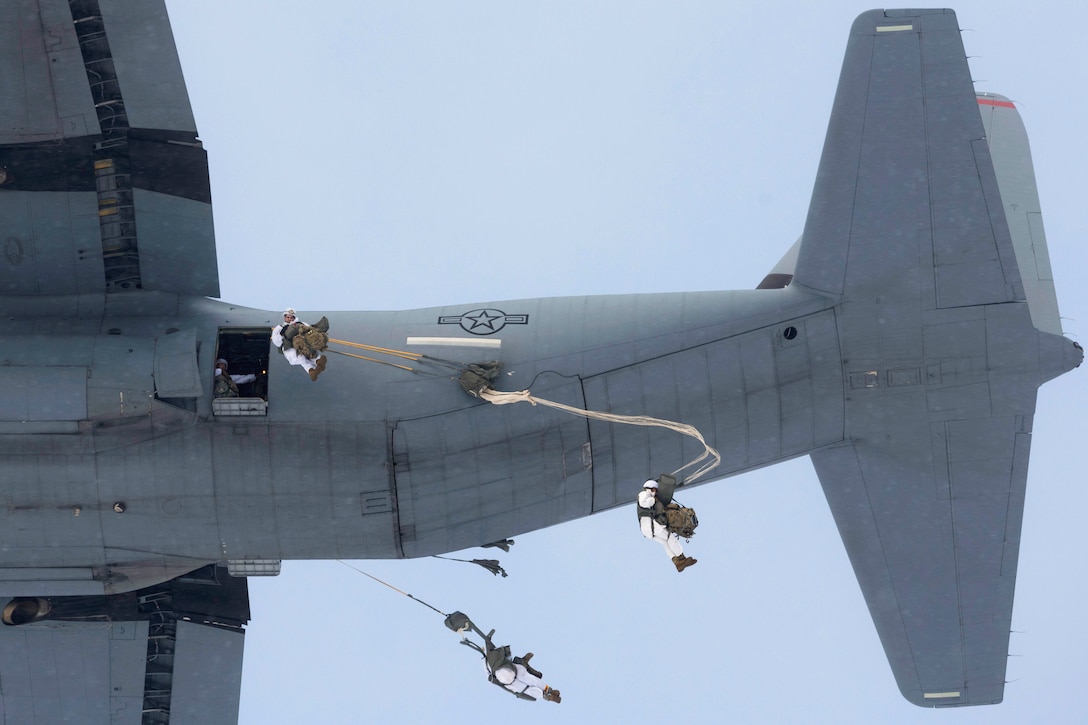 Soldiers jump from an aircraft with parachutes.