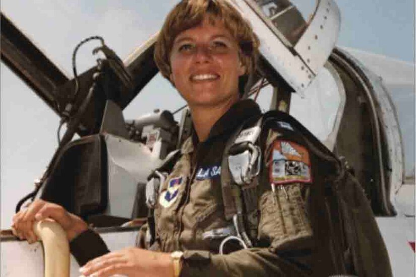 An airman poses for a photo in front of an aircraft.