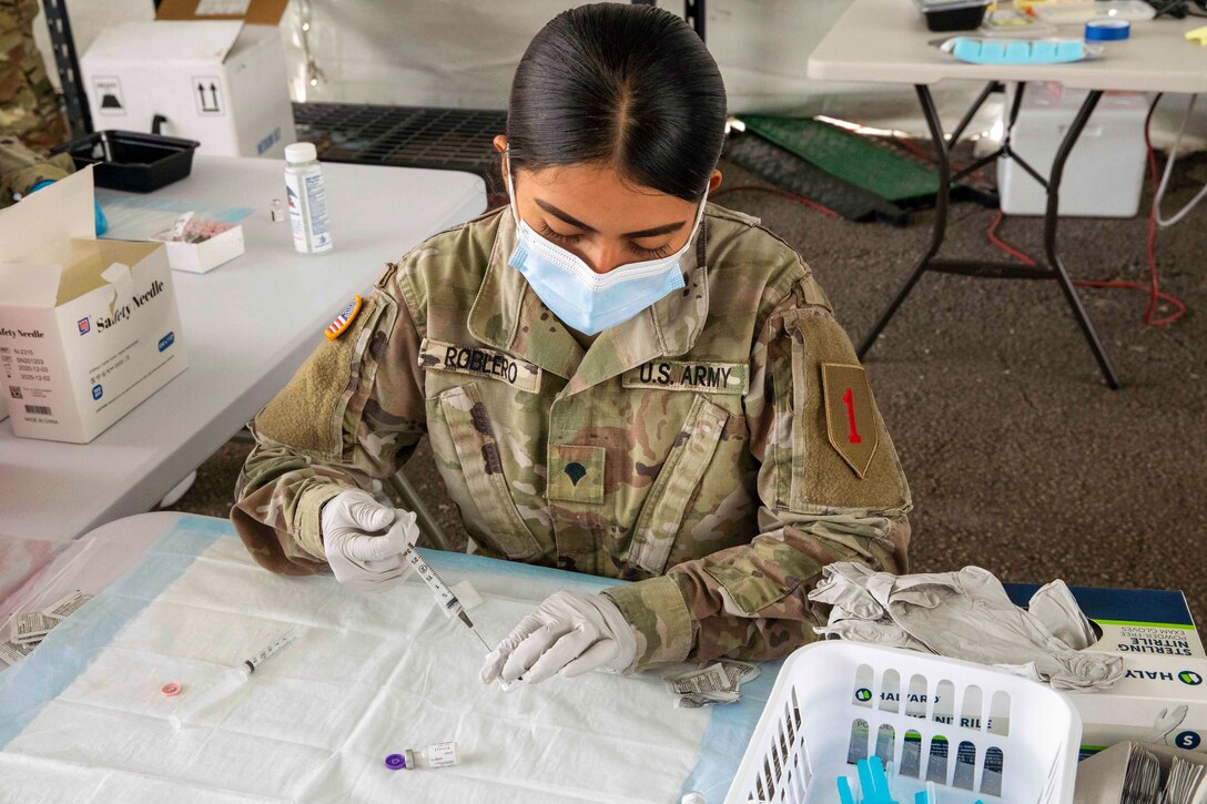 A soldier uses a syringe to pull the COVID-19 vaccine from a vial.