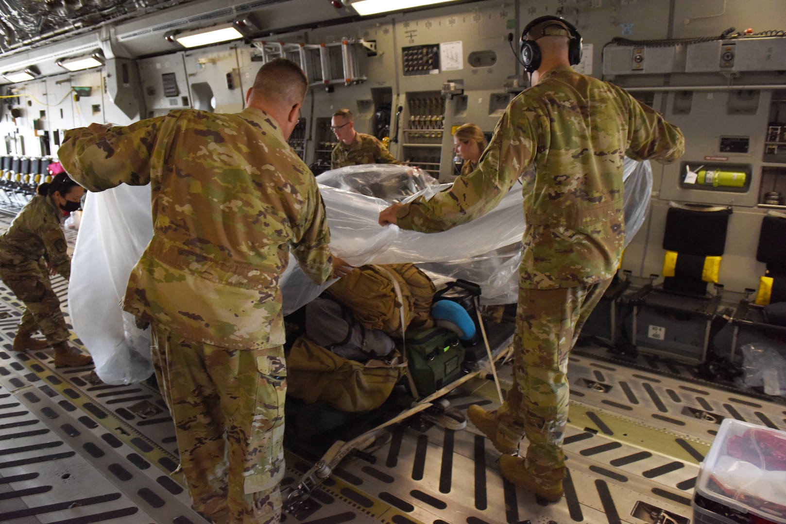 U.S. Air Force Airmen from the 775th Expeditionary Aeromedical Evacuation flight from Travis Air Force Base, California, cover their luggage and equipment with a plastic tarp aboard a C-17 Globemaster III on Joint Base Lewis-McChord, Washington, March 31, 2021. They covered their equipment and luggage with plastic in preparation for a COVID-19 patient who was being flown to San Antonio Army Medical Center in Texas. (U.S. Air Force photo by Senior Airman Mikayla Heineck)