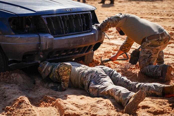 Airmen in the dirt with shovels dig underneath car.