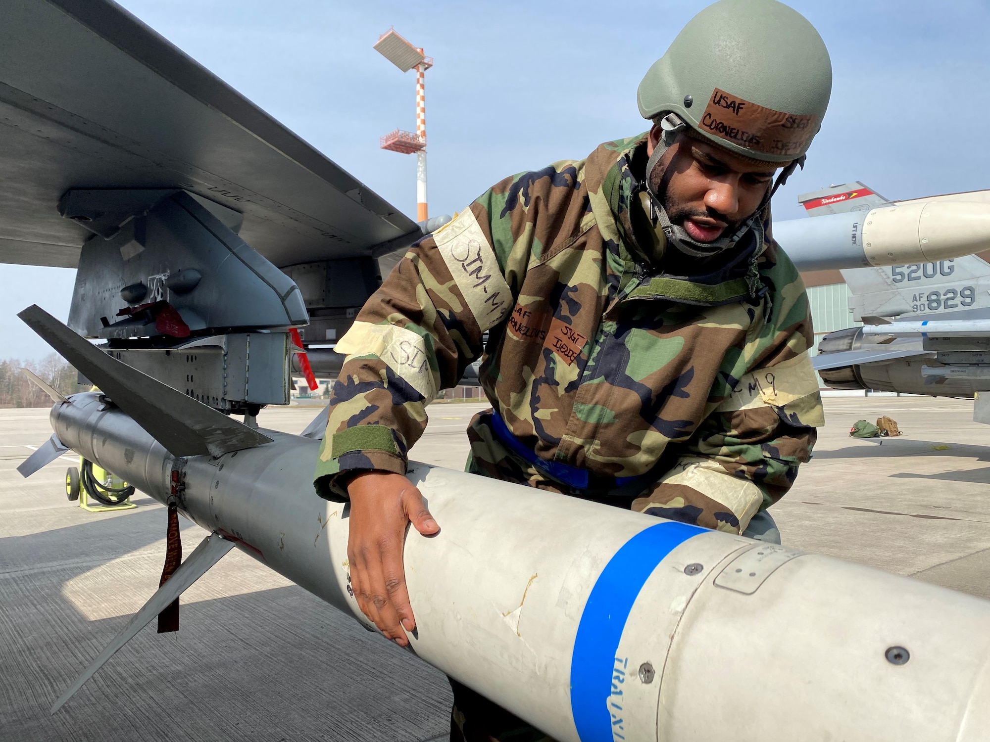 U.S. Air Force Staff Sgt. Cornelius Ijezie, a 52nd Maintenance Squadron Munitions Stockpile Supervisor, inspects a munition on an U.S. Air Force F-16 Fighting Falcon, while in Mission Oriented Protective Posture gear during an ACE exercise at Ramstein Air Base Germany, March 25, 2021. ACE, is Agile Combat Employment, an operational concept that allows forces to generate sorties from various locations with the support of multi-capable Airmen. (U.S. Air Force photo by Tech Sgt. Warren Spearman Jr.)