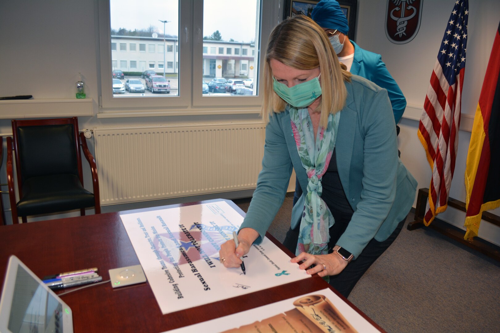 Julia Armstrong, the Sexual Harassment/Assault Response and Prevention Program Manager for Regional Health Command Europe, signs a poster that RHCE employees will not tolerate sexual harassment and sexual assault.