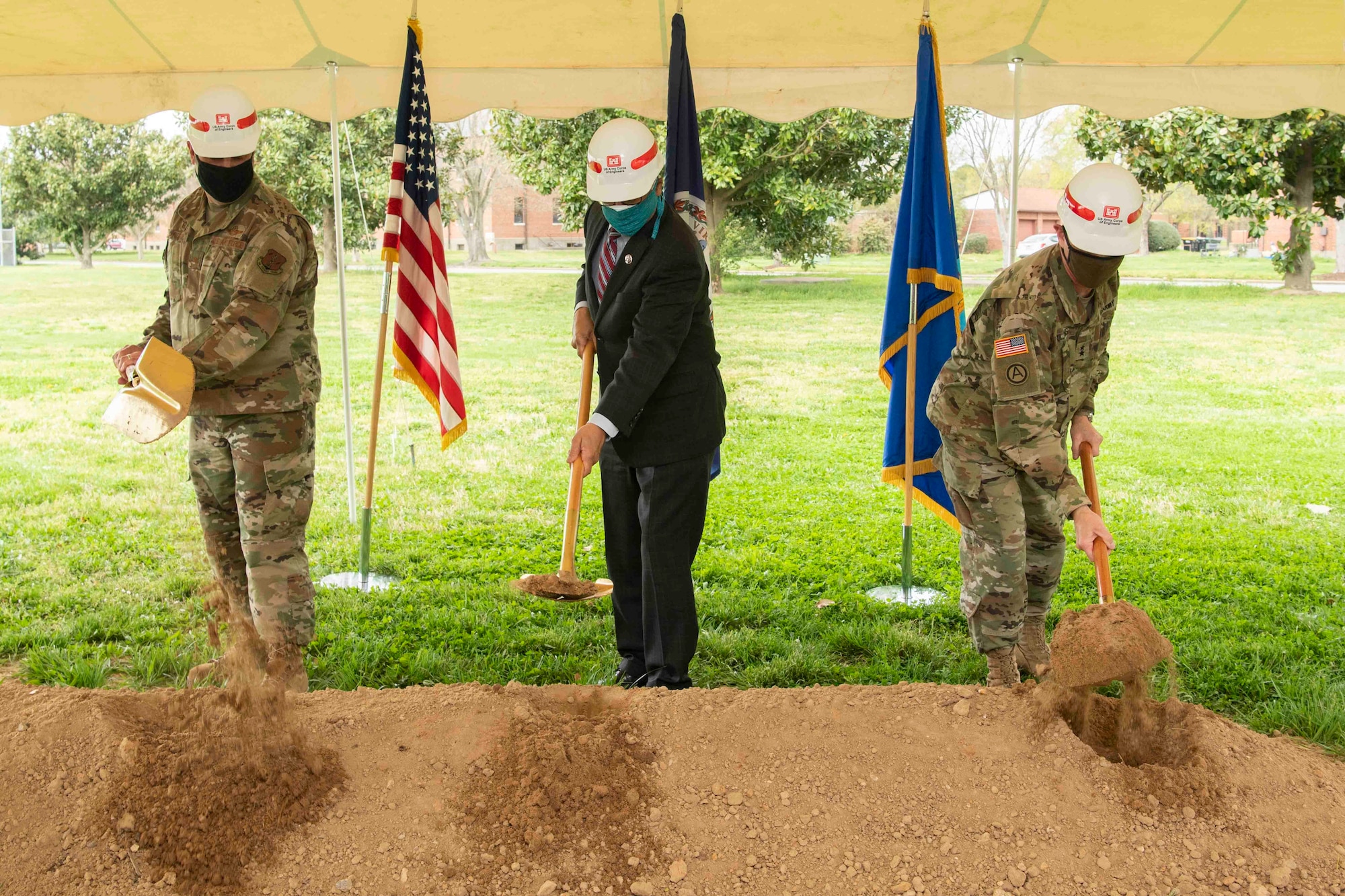 Three men wearing hard hats ceremoniously turn dirt during a ground breaking ceremony