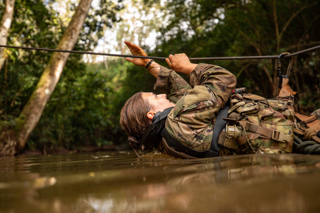A soldier immersed in water crosses a river with a rope.