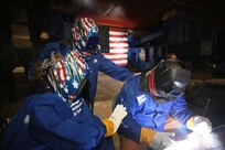 The future the future USS Harvey C. Barnum, Jr. (DDG 124) namesake, Col. Harvey "Barney" Barnum, Jr. (USMC, Ret.) (center) and his wife and ship sponsor, Martha Hill (left) monitor as Bath Iron Works welder Marty Fish (right) inscribes Col. Barnum’s  signature onto the keel plate at General Dynamics Bath Iron Works (BIW) shipyard, April 6.