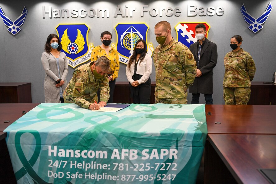 Col. Katrina Stephens, installation commander, signs a Sexual Assault Awareness and Prevention Month proclamation at Hanscom Air Force Base, Mass., March 30, while Staff Sgt. Samantha Marchionda, from left, Rachel Desharnais, Jersouk Touy, Chief Master Sgt. William Hebb, installation command chief,  Staff Sgt. David Ahn and Master Sgt. Jessica Subia, members of the Sexual Assault Prevention Response Office, look on. April is Sexual Assault Awareness and Prevention Month.  (U.S. Air Force photo by Mark Herlihy)