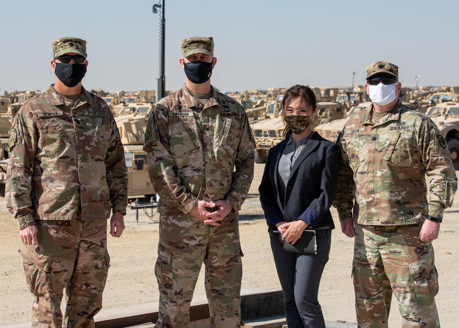 Three masked male military officers stand with a female masked civilian at Camp Arifjan, Kuwait.