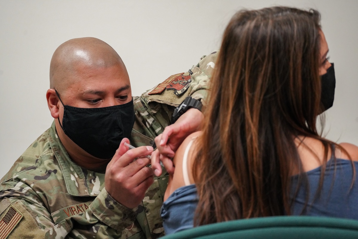 A U.S. Air National Guard member gives a COVID-19 vaccination into the arm of a military dependent.
