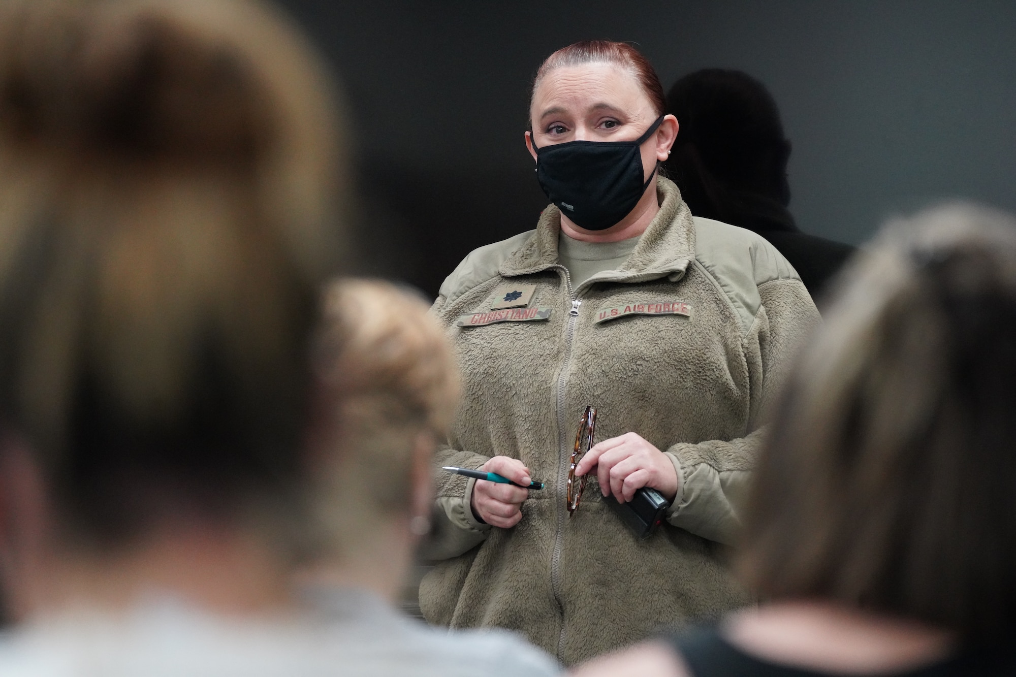 A U.S. Air National Guard member standing in front of a group of military dependents inside a medical waiting room while answering questions about the COVID-19  vaccine.