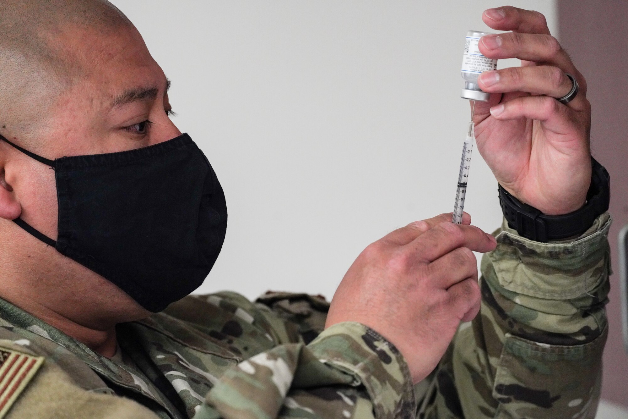 A U.S. Air National Guard member injects a syringe into a vile of the Moderna COVID-19 vaccine.