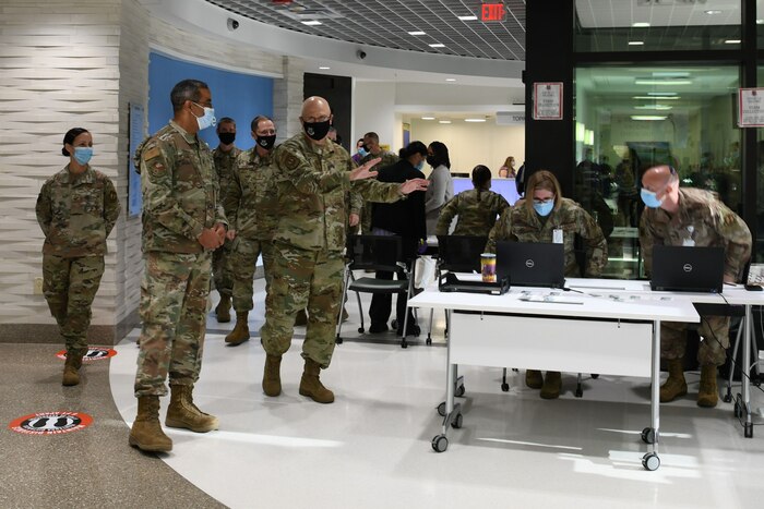 Photo shows the command team being led by tables manned by personnel near an entrance to the hospital.