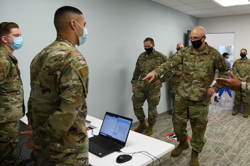 Photo shows command team speaking to two Airman standing behind computers.