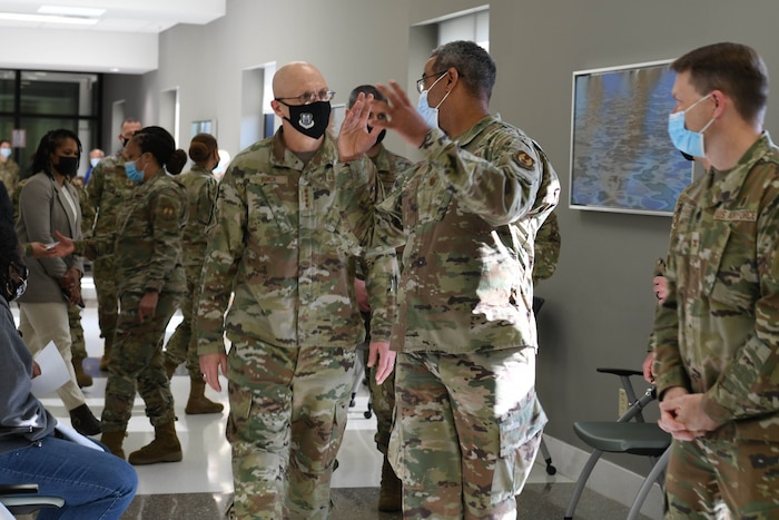 Photos shows the general walking through a hallway with people seated on either side.