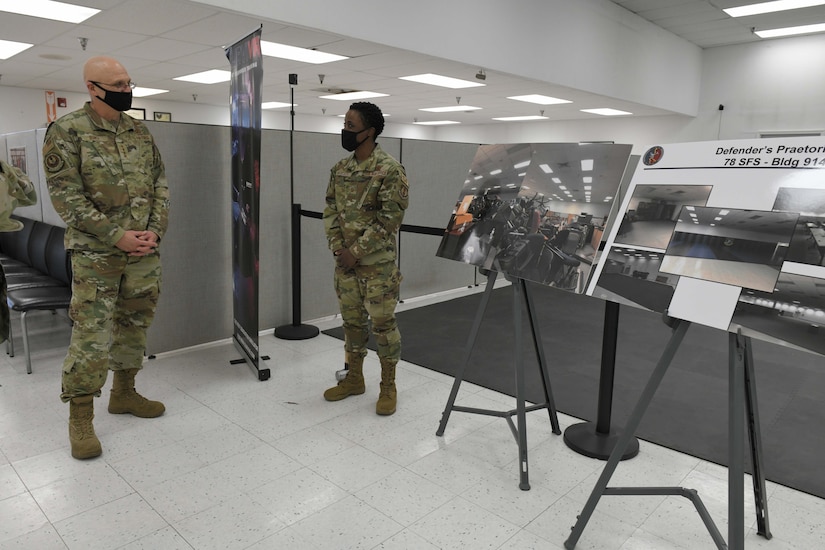 Photo shows the general looking at two informational boards while an Airman speaks to him.