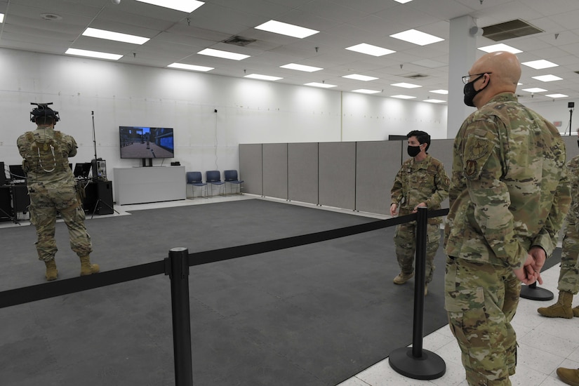 Photo shows the general watching an individual using a VR device on his head.