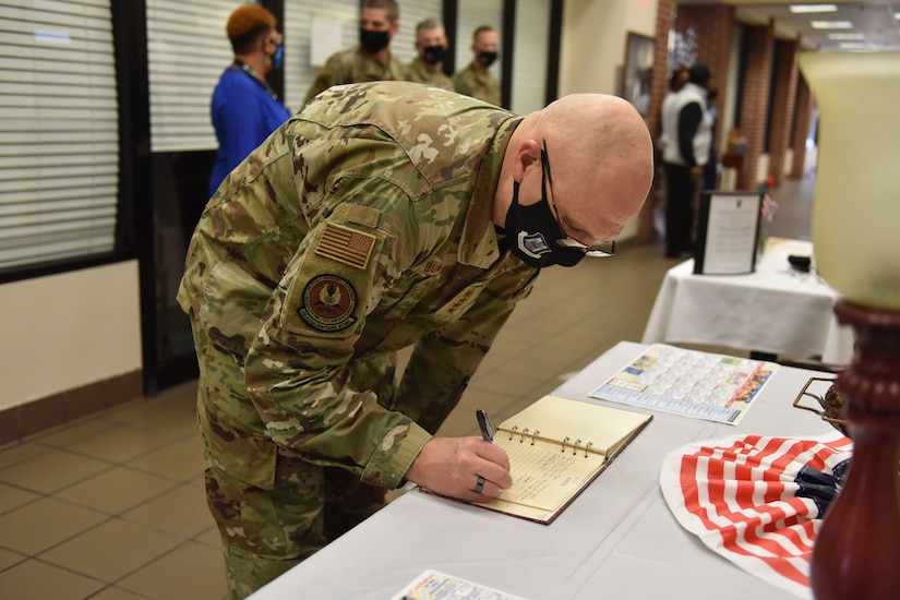 Photo shows the general signing a book on a table.