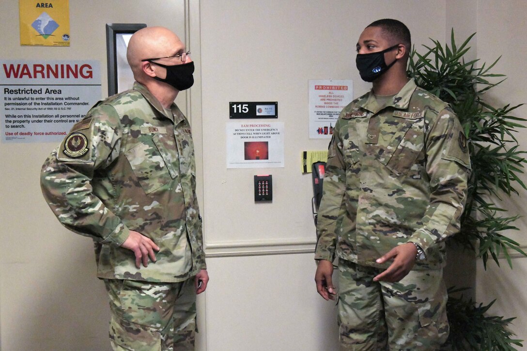 Photo shows two men standing in an entryway speaking to one another.