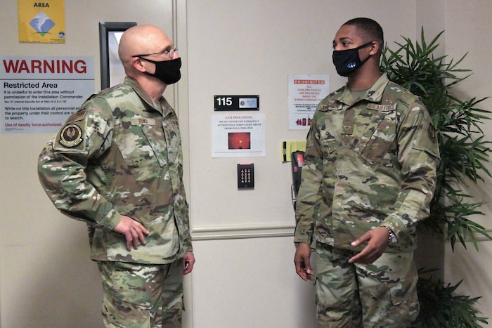 Photo shows two men standing in an entryway speaking to one another.